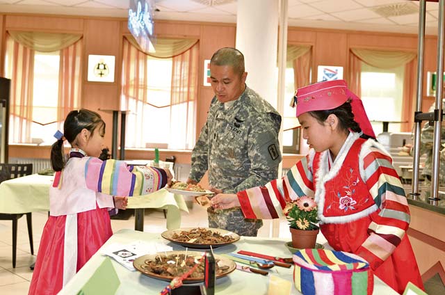 Photo by Ignacio “Iggy” Rubalcava An Asian-Pacific experience Dressed in traditional Korean attire, Yein Lee (left) and Yeji Lee serve beef bulgogi to Sgt.  Major Jose A. Santiago from the 421st Multifunctional Medical Battalion during Baumholder’s Asian-Pacific Heritage Month commemoration May 30. Santiago was the guest speaker during the luncheon. Yein, her sister, Yeji, and their father, Spc. William Hilton, also participated in the program with a brief presentation about Korean culture titled “Asian-Pacific Experience.”
