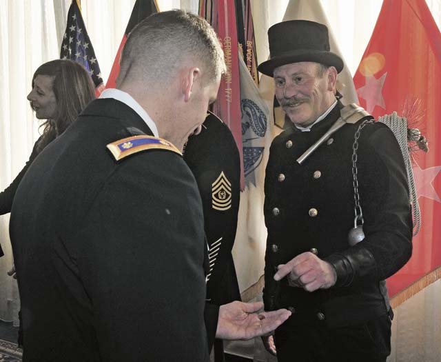 Thomas Scharwatz, a chimney sweeper from Clausen, Germany, presents Maj. Christopher Bachman, the  21st Theater Sustainment Command chief of Operations Research System Analysis section, with a one euro cent coin during the 21st TSC New Year’s Reception Jan. 10 at Armstrong’s Club on Vogelweh.