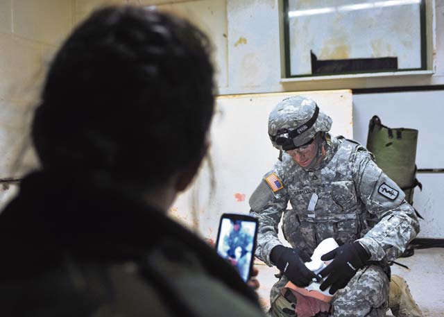 Bulgarian Sgt. Maj. Teodora Kodzhabasheva (left) films Pfc. Travis W. Sinfellow, combat  medic assigned to the 21st Theater Sustainment Command’s 557th Medical Company, 421st Multi-Medical Battalion, 30th Medical Brigade, while he applies a bandage to the severed limb of a training dummy during a military-to-military training exchange  Feb. 11 on Smith Barracks in Baumholder.