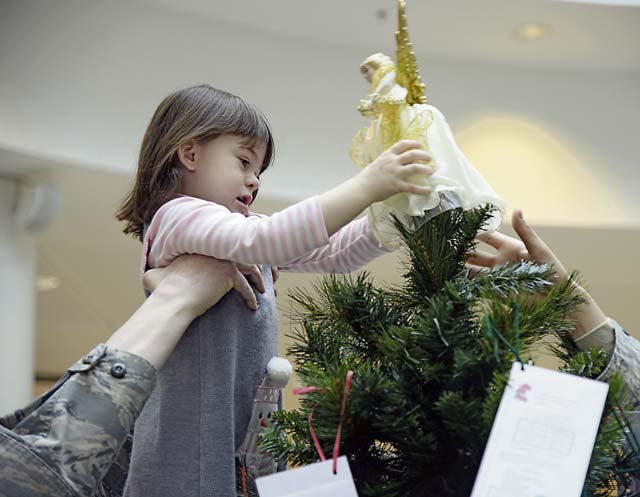 Master Sgt. Timothy Bliefnick, 86th Comptroller Squadron and Wing Staff Agencies first sergeant, helps his daughter, Annabella, place an angel decoration on top of a tree in the Kaiserslautern Military Community Center Nov. 17 on Ramstein. The 13 trees set up around the KMC to accept donations are meant to be used to provide financial relief to military families during the holiday season.