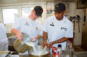Spc. Caleb Morse  (left) and Sgt.  Herman Smith whip up a container of alfredo sauce for the lunch meal at the Patriot Garden dining facility March 24 on Rhine Ordnance Barracks. The staff enjoys cooking themed meals for diners each week.