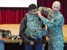Col. Matthew Redding, 21st Theater Sustainment Command chief of staff, helps a student don military protective armor during the resiliency forum. The chief subsequently directed the student to run across the room and do pushups.