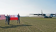U.S. and Polish military members hold flags as a C-130J Super Hercules assigned to the 37th Airlift Squadron performs a grass-strip landing at Powidz Air Base, Poland, April 10.