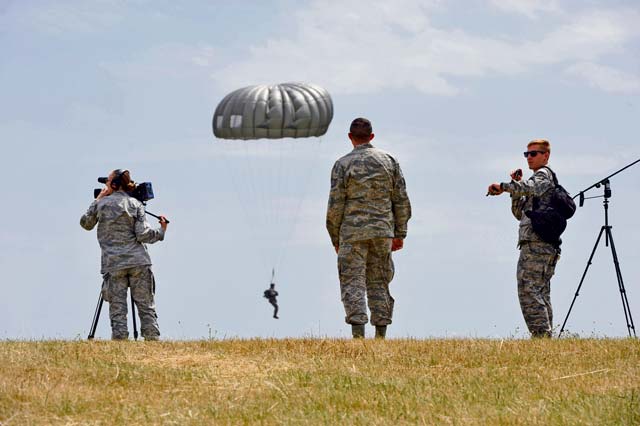 Photo by Staff Sgt. Leslie Keopka  Supporting units watch as paratroopers disembark from a C-130J Super Hercules and land nearby during International Jump Week near Alzey, July 7. During jump week, more than 200 U.S. and allied partners exited their designated aircrafts as paratroopers to strengthen and hone procedures and tactics. Supporting units included Air Force and Army medical personnel, air traffic controllers and land navigators.