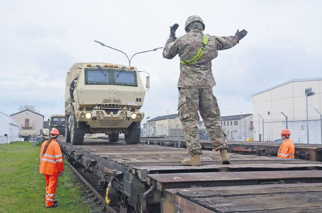 Sgt. James Gross, 3rd Infantry Division, guides a vehicle into position on a train car at Coleman Work Site, Mannheim, while “Deutsche Bahn,” meaning “German Rail,” members look on.