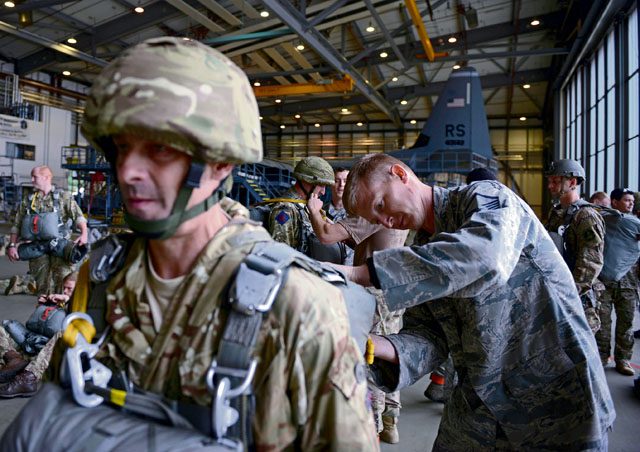 Photo by Airman First Class Joshua Magbanua Master Sgt. Benjamin Thomas, 435th Contingency Response Support Squadron training flight chief, assists a British paratrooper with his gear before an airborne operation during International Jump Week July 28 on Ramstein. 