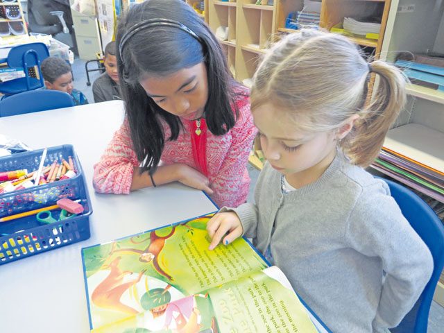Kyla Mae Jornacion, fifth-grader in Maxine Reid’s class (left), and Megan Cornfeld, first-grader in Gabriele Arseneault’s class, read about a zoo in the park during a multiage partial German immersion class Sept. 28 at Landstuhl Elementary Middle School. Once a week, the fifth-graders and the first- and second-graders come together to read or write, allowing students to connect with each other across grade levels.