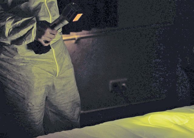 An Air Force Office of Special Investigations 4th Field Investigations Squadron agent utilizes an alternate light source during a mock crime scene Oct. 6 on Ramstein. Agents may select from six different light sources to search for biological fluids undetectable to the naked eye.