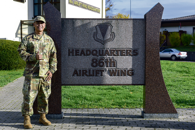 U.S. Air Force Tech. Sgt. MC Garrette Dela Cruz, 86th Airlift Wing administrative executive non-commissioned officer in charge, stands next to the 86th AW headquarters building sign at Ramstein Air Base, Germany, Nov. 16, 2022. Dela Cruz was recently awarded Airlifter of the Month for the hard work and dedication to his unit and for investing in the community as a task force leader for Armed Forces Against Drunk Driving and facilitating the most recent Ramstein Enlisted Summit. (U.S. Air Force photo by Airman 1st Class Madelyn Keech)